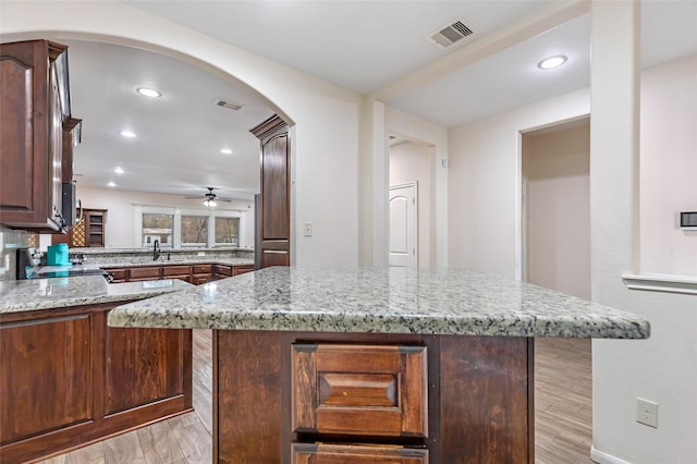 kitchen with light stone countertops, a center island, stove, and sink