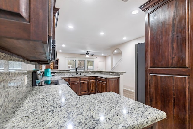 kitchen featuring light stone countertops, stainless steel range oven, kitchen peninsula, and sink