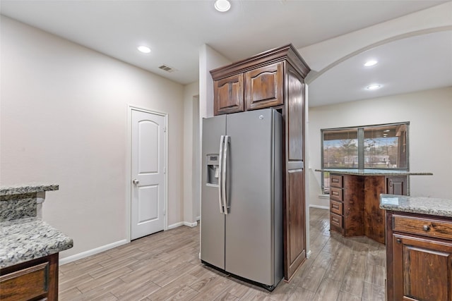 kitchen with stainless steel refrigerator with ice dispenser, dark brown cabinetry, and light stone counters