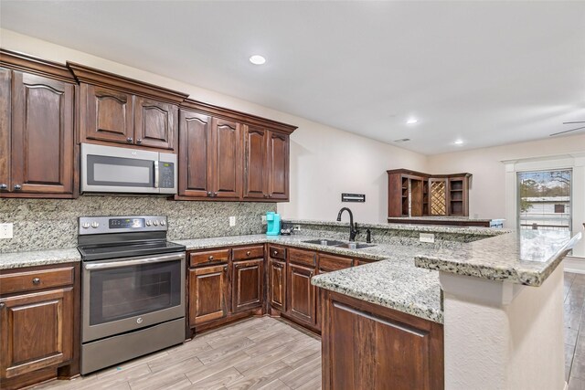 kitchen with kitchen peninsula, sink, appliances with stainless steel finishes, and light hardwood / wood-style flooring