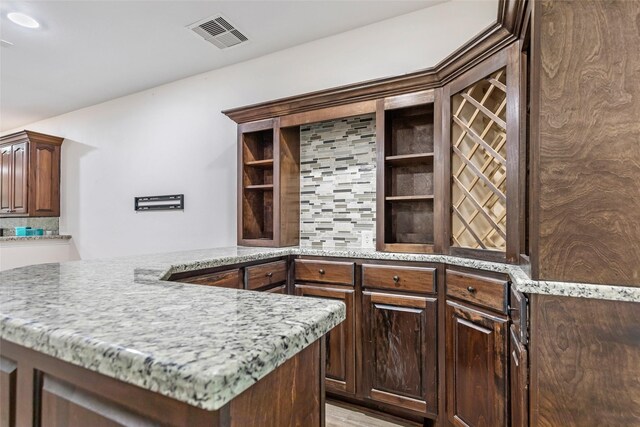 kitchen featuring backsplash, dark brown cabinetry, light stone countertops, and kitchen peninsula