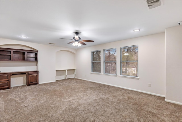 unfurnished living room with ceiling fan, built in desk, and carpet floors