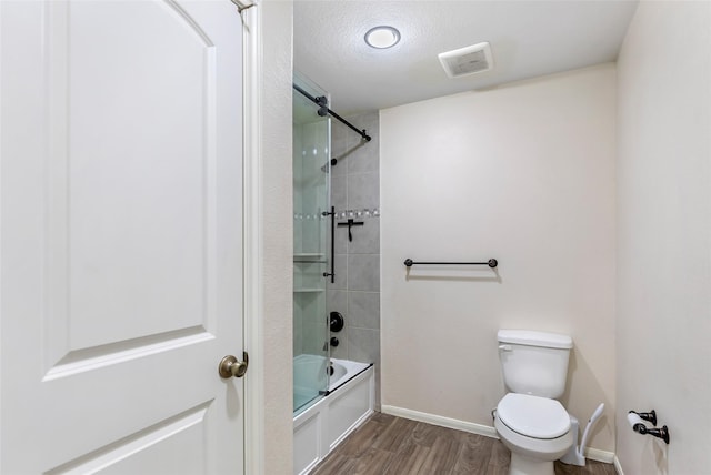 bathroom featuring hardwood / wood-style floors, toilet, bath / shower combo with glass door, and a textured ceiling