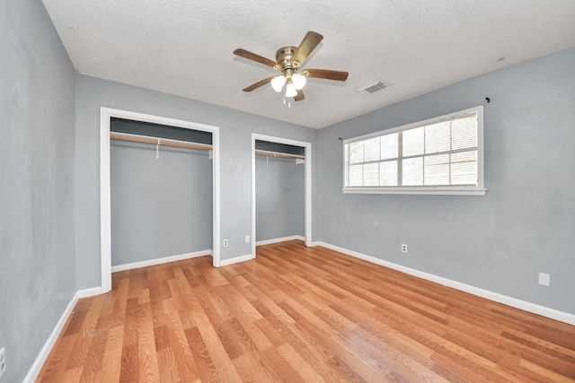 unfurnished bedroom with a textured ceiling, light wood-type flooring, two closets, and ceiling fan