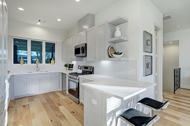 kitchen with sink, a kitchen breakfast bar, light hardwood / wood-style flooring, backsplash, and appliances with stainless steel finishes