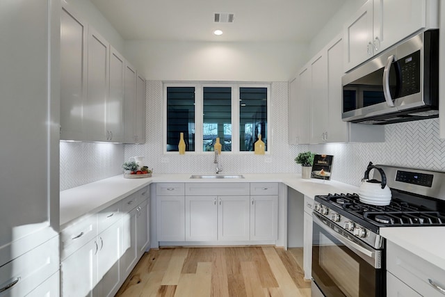 kitchen featuring white cabinets, sink, decorative backsplash, light wood-type flooring, and appliances with stainless steel finishes