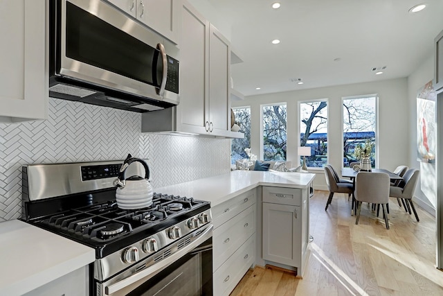 kitchen featuring kitchen peninsula, appliances with stainless steel finishes, light wood-type flooring, tasteful backsplash, and white cabinetry