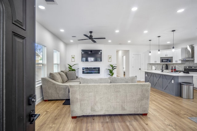 living room with light wood-type flooring, ceiling fan, and sink