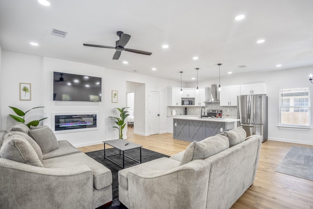 living room featuring light hardwood / wood-style flooring, ceiling fan, and sink