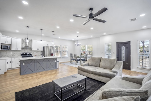 living room featuring ceiling fan with notable chandelier, light wood-type flooring, and sink