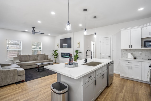 kitchen with a kitchen island with sink, sink, dishwasher, white cabinetry, and hanging light fixtures