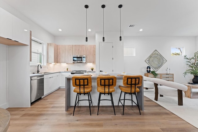 kitchen featuring stainless steel appliances, light hardwood / wood-style flooring, a center island, white cabinetry, and hanging light fixtures