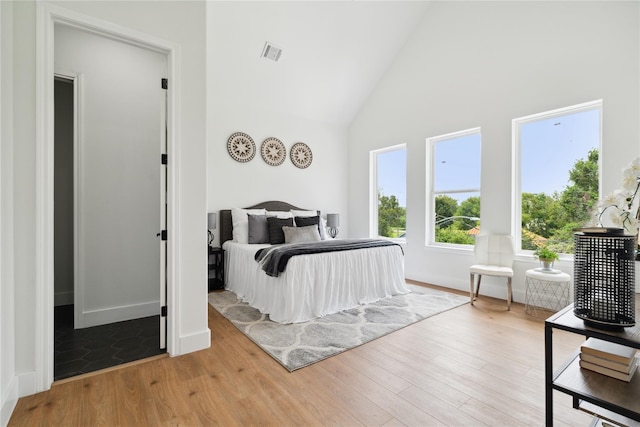 bedroom with light wood-style floors, baseboards, visible vents, and high vaulted ceiling