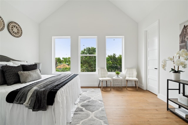 bedroom featuring high vaulted ceiling, light wood-style flooring, and baseboards