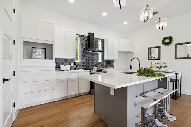 kitchen featuring light countertops, white cabinets, a kitchen island with sink, wall chimney range hood, and stainless steel electric range