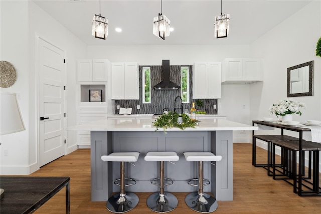 kitchen with light countertops, a center island with sink, and wall chimney exhaust hood