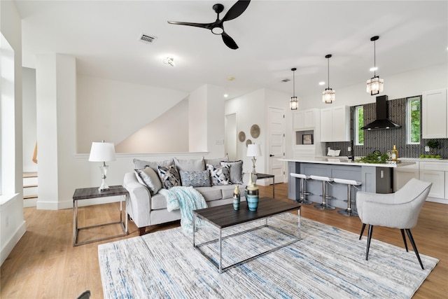 living area featuring a ceiling fan, light wood-type flooring, visible vents, and baseboards