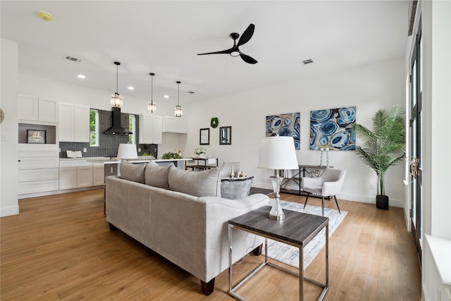 living room with light wood-style floors, visible vents, baseboards, and a ceiling fan