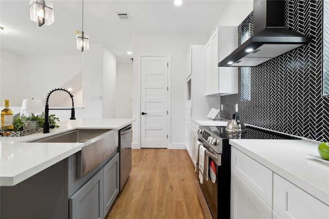 kitchen with wall chimney exhaust hood, hanging light fixtures, light countertops, and stainless steel appliances