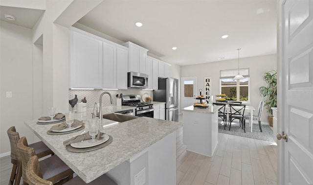 kitchen with kitchen peninsula, appliances with stainless steel finishes, a kitchen bar, sink, and decorative light fixtures