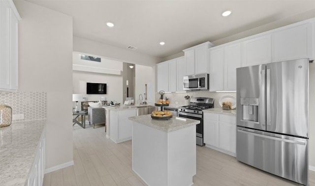 kitchen with light stone countertops, stainless steel appliances, a kitchen island, and white cabinets