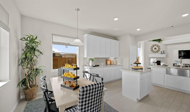 kitchen featuring white cabinets, sink, decorative backsplash, decorative light fixtures, and a kitchen island