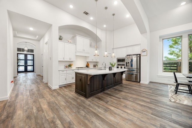 kitchen featuring a center island with sink, white cabinets, appliances with stainless steel finishes, decorative light fixtures, and a kitchen bar