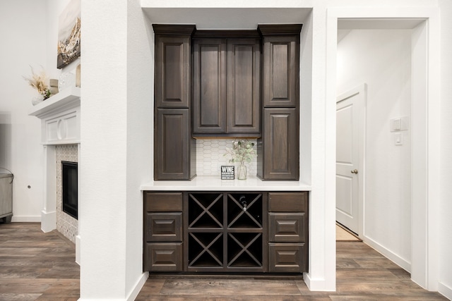 bar with a fireplace, dark brown cabinets, dark hardwood / wood-style flooring, and backsplash