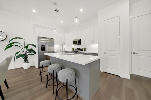 kitchen with white cabinets, sink, hanging light fixtures, an island with sink, and stainless steel appliances