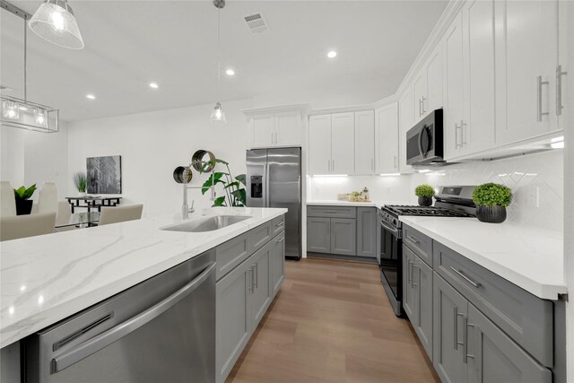 kitchen featuring appliances with stainless steel finishes, sink, gray cabinets, white cabinetry, and hanging light fixtures