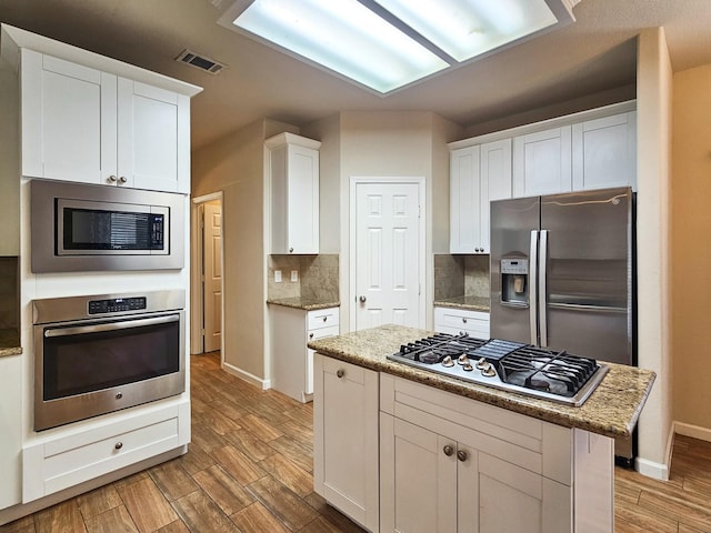 kitchen featuring light stone countertops, white cabinetry, a center island, stainless steel appliances, and decorative backsplash