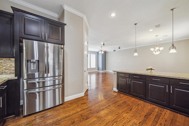 kitchen with light stone countertops, tasteful backsplash, stainless steel fridge, ceiling fan with notable chandelier, and ornamental molding