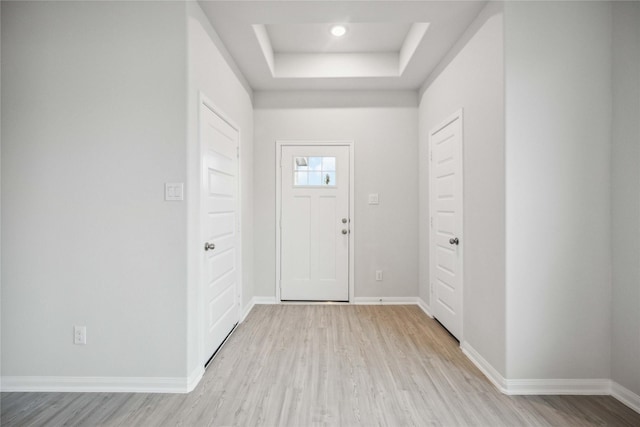 entryway with light wood-type flooring and a tray ceiling