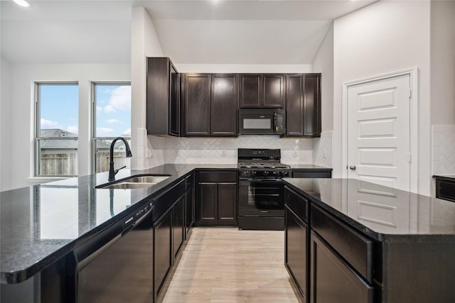 kitchen with sink, dark stone counters, a kitchen island, black appliances, and light wood-type flooring