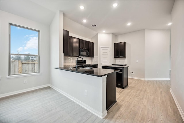 kitchen with kitchen peninsula, decorative backsplash, light wood-type flooring, sink, and black appliances