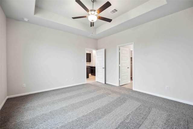 unfurnished bedroom with a raised ceiling, ensuite bath, ceiling fan, and light carpet