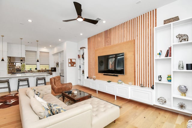 living room with ceiling fan, light hardwood / wood-style flooring, and built in shelves