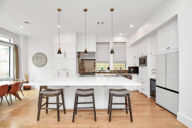 kitchen with white cabinetry, built in appliances, a large island, and a breakfast bar area