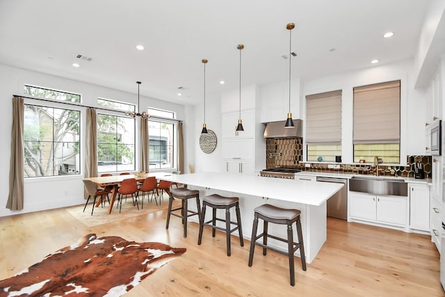 kitchen with sink, hanging light fixtures, a kitchen island, stainless steel dishwasher, and white cabinets