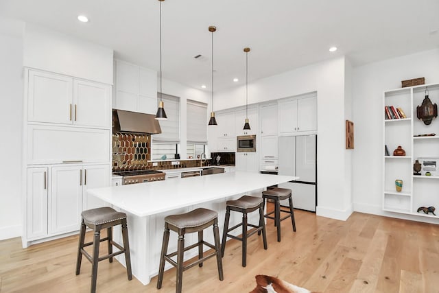 kitchen with decorative light fixtures, built in appliances, a spacious island, and wall chimney exhaust hood