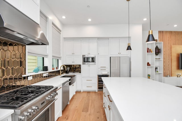 kitchen with white cabinets, pendant lighting, built in appliances, and wall chimney exhaust hood