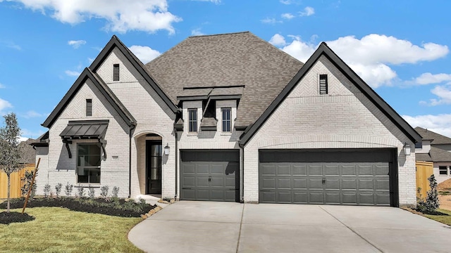 french country home with brick siding, an attached garage, a shingled roof, a front yard, and driveway