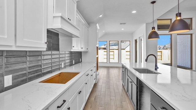 kitchen with tasteful backsplash, white cabinets, light stone counters, and a sink