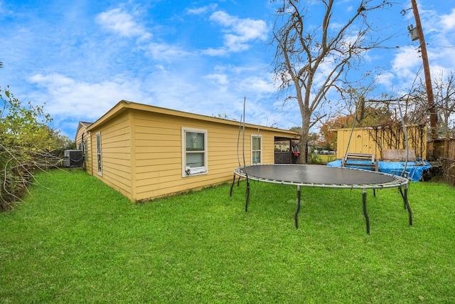 back of property with a trampoline, a yard, and central air condition unit