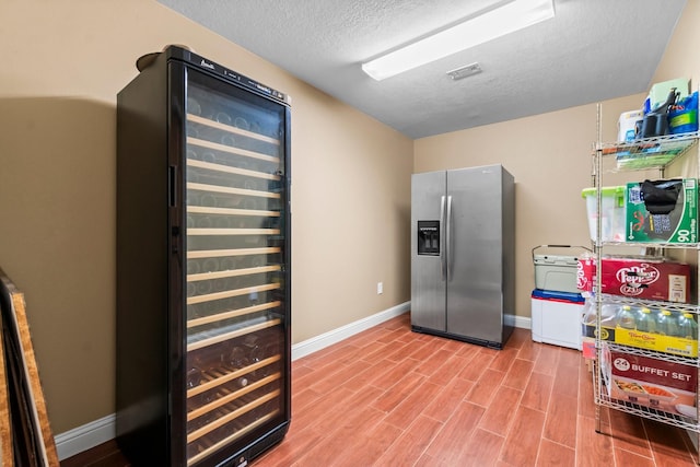 kitchen featuring wine cooler, stainless steel fridge with ice dispenser, and a textured ceiling