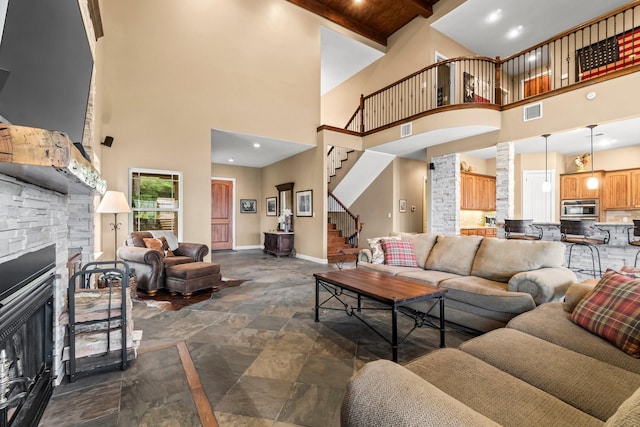 living room with a stone fireplace, a towering ceiling, beam ceiling, wood ceiling, and decorative columns