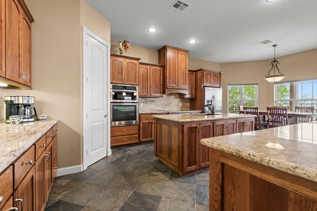 kitchen with tasteful backsplash, stainless steel appliances, a kitchen island with sink, sink, and decorative light fixtures