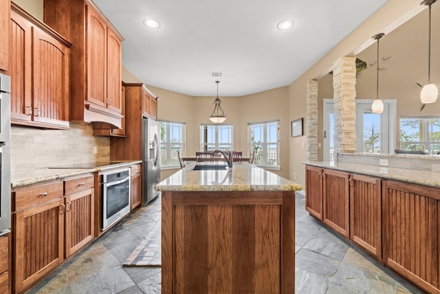 kitchen featuring a kitchen island with sink, sink, hanging light fixtures, decorative backsplash, and appliances with stainless steel finishes