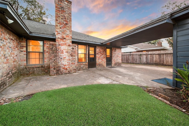 back house at dusk with a yard and a patio