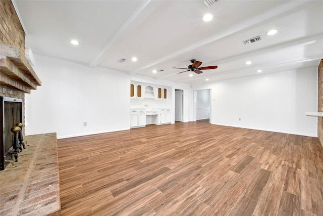 unfurnished living room featuring beam ceiling, a fireplace, built in desk, and light wood-type flooring